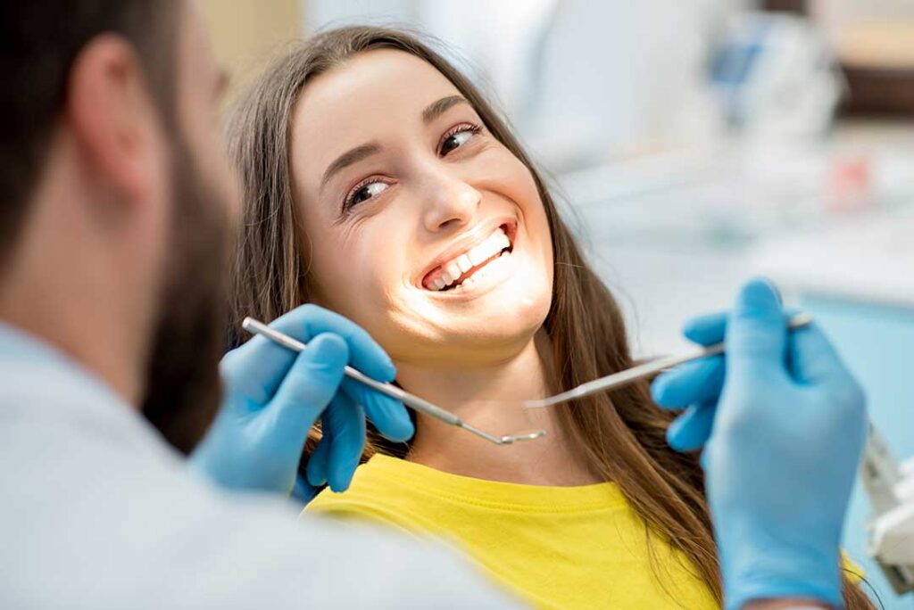 A person using a tongue scraper while standing at a bathroom sink with a toothbrush nearby.